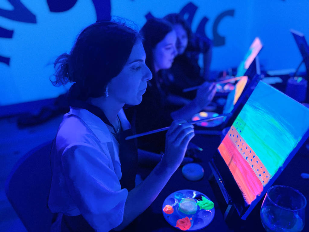 Un primo piano di una persona che dipinge con colori al neon sotto le luci UV