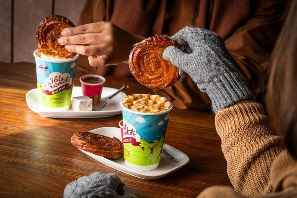 a hand dipping a salted caramel cronut into a hot chocolate for the hot chocolate festival