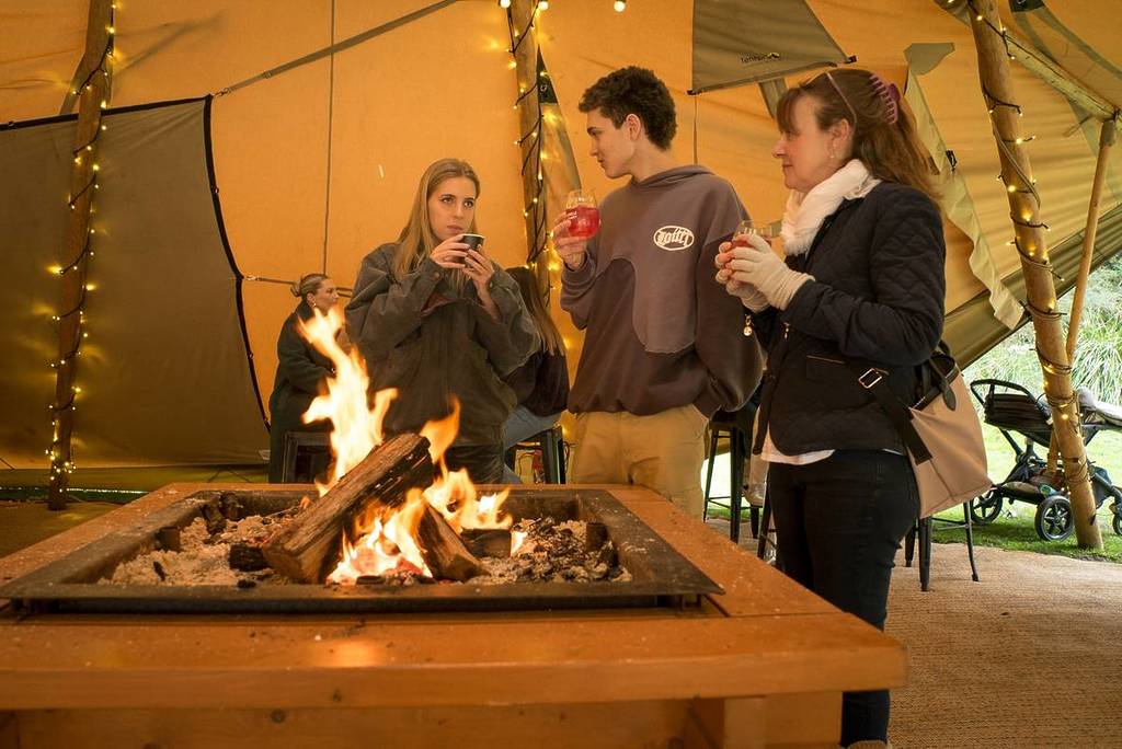 people sipping wine by a fire under a tepee at Wine & Wildlife