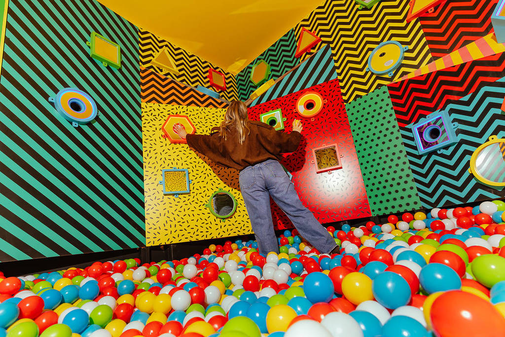 woman pressing buttons on wall standing in a colourful ball pit at Hijinx Hotel in QV