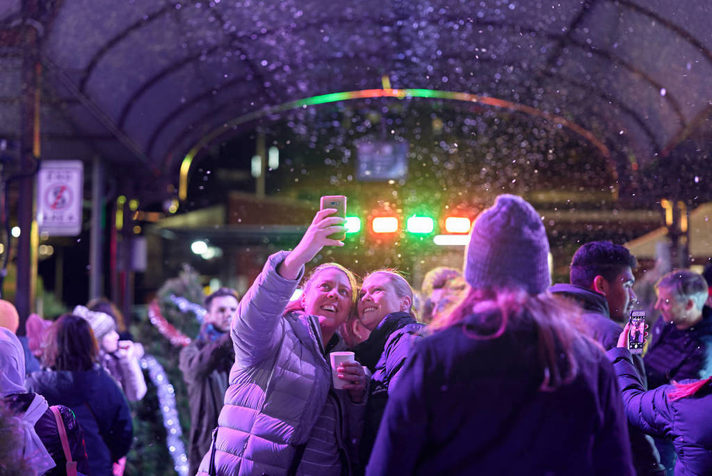 people taking photos at Queen Victoria Market's Winter Night Market underneath falling snow