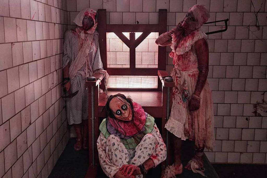 Three figures dressed up in white clothing covered with blood pose in a cell at Prison Island.