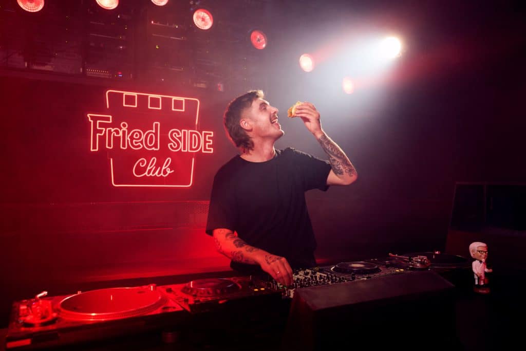 man about to eat a KFC slider in front of a DJ controller