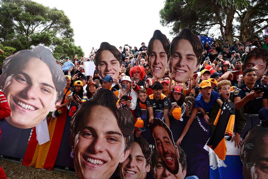 crowd of fans holding cardboard cutouts of race car drivers faces at F1 Australian Grand Prix