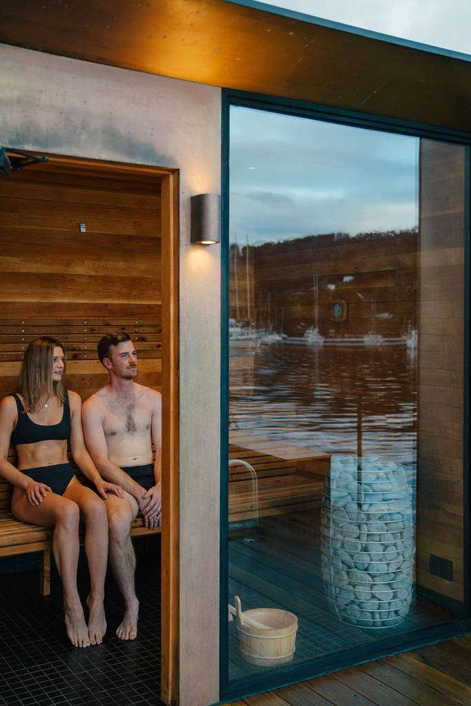 couple sitting inside a sauna on the boat, with the window reflection showing surrounding water