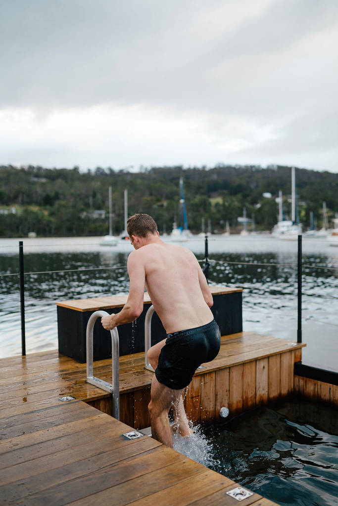 man climbing down ladder into ice bath on a boat
