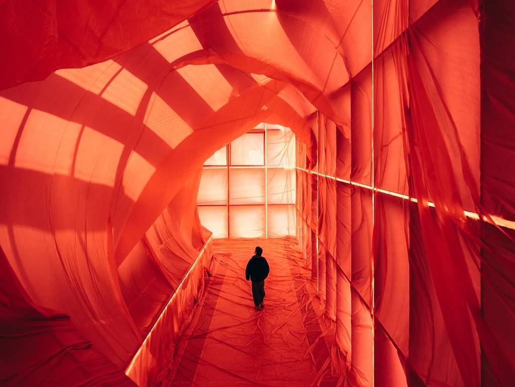 man walking in corridor surrounded by red fabric, one of the art installations for Now or Never festival