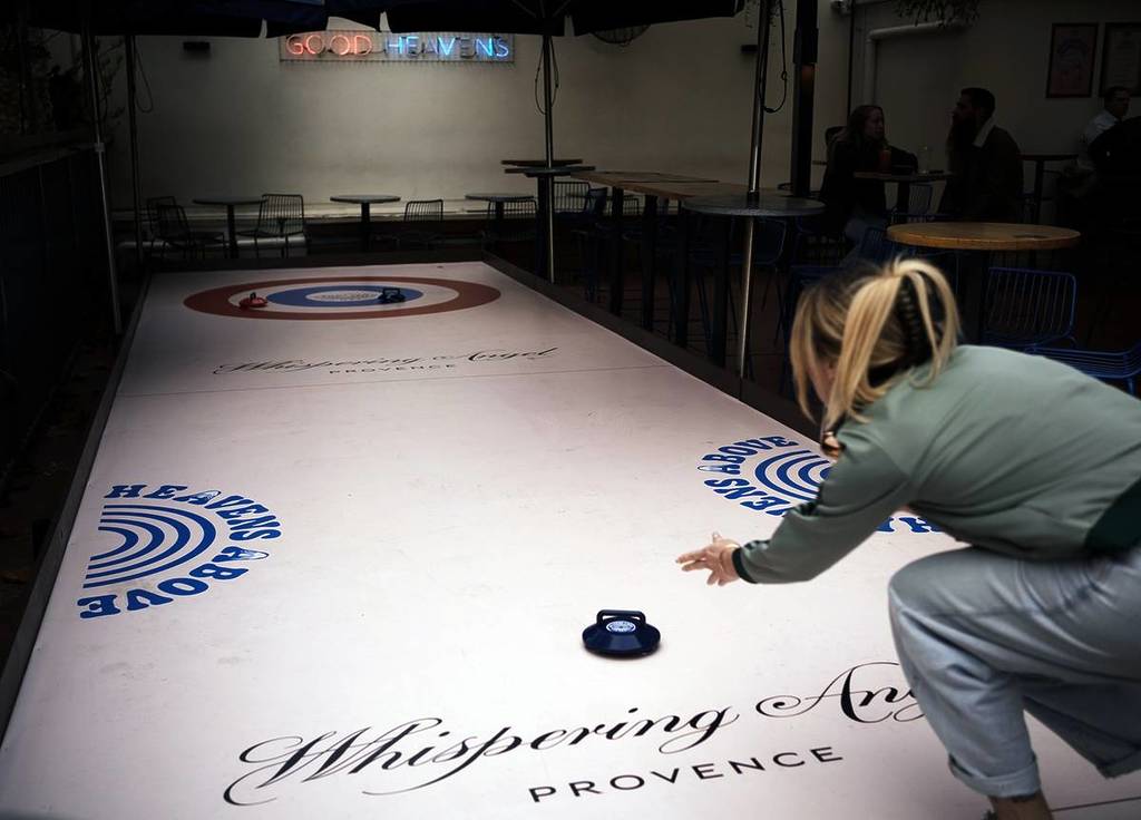 A woman throws a Kurling stone at the rooftop rink at Good Heavens.