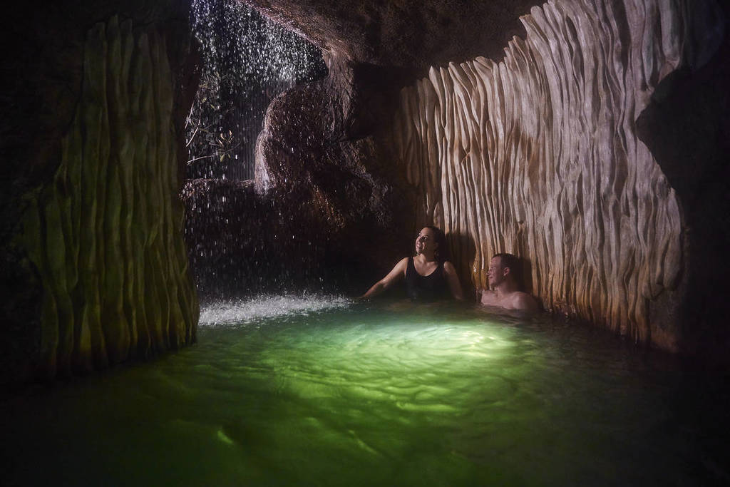 a couple in a cave area of Deep Blue Hot Springs, with glowing lights beneath them and a gentle waterfall at the cave entrance