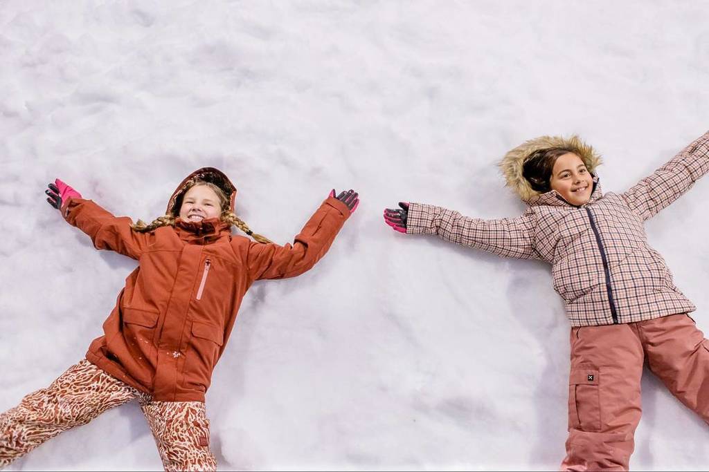 Two children lie in snow making snow angels.