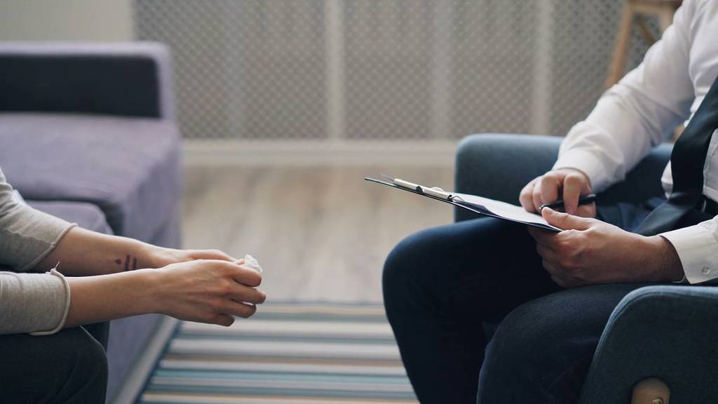 woman's hand holding tissues while man's hands hold clipboard, depicting people listening for the Mental Health and Wellbeing Locals support system