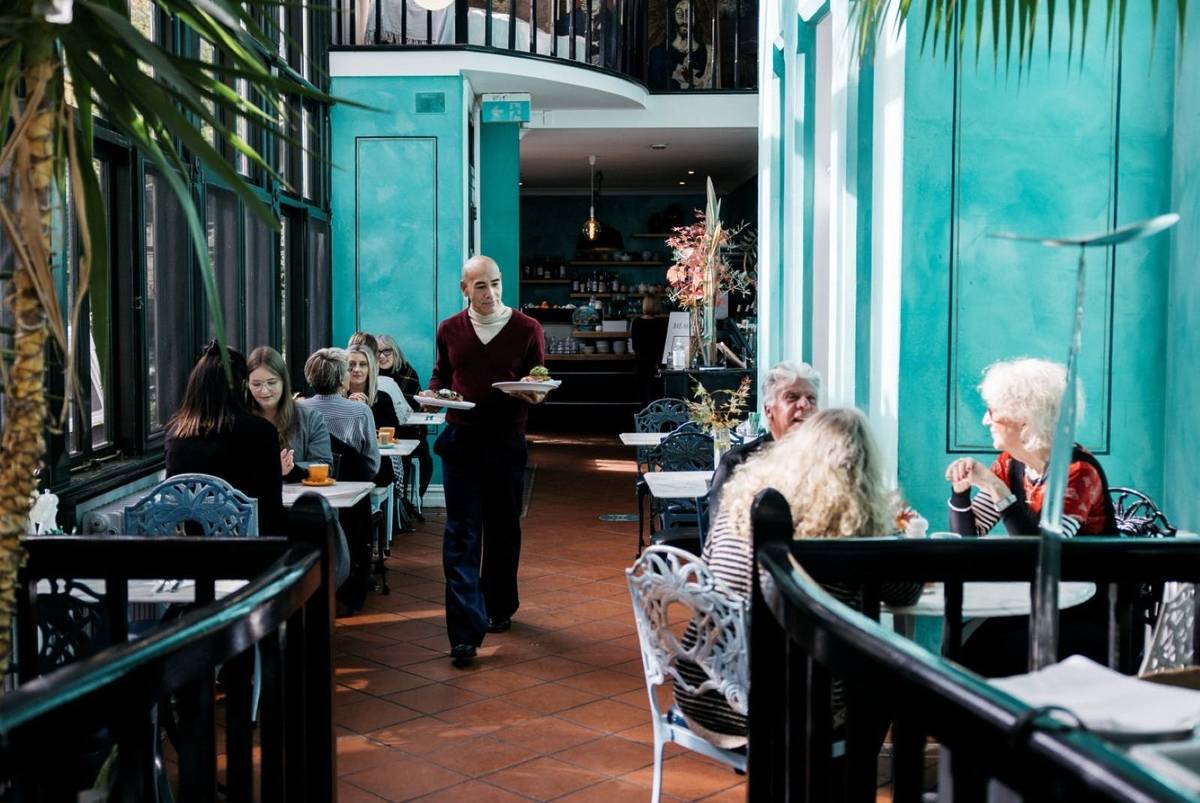 Interior of Bad Habits cafe in Daylesford, with patrons enjoying meals and a waiter serving food in a bright, turquoise-themed space