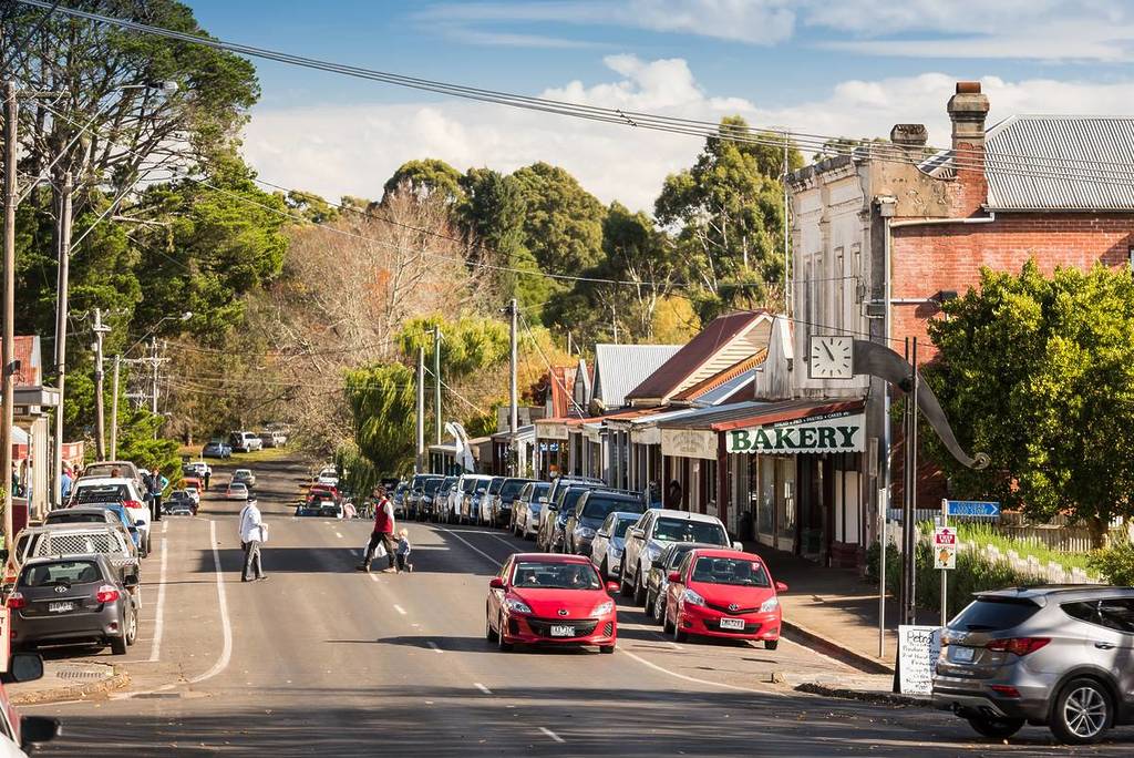 High Street in Trentham, Victoria, with parked cars, pedestrians crossing, and a row of historic shopfronts including a bakery