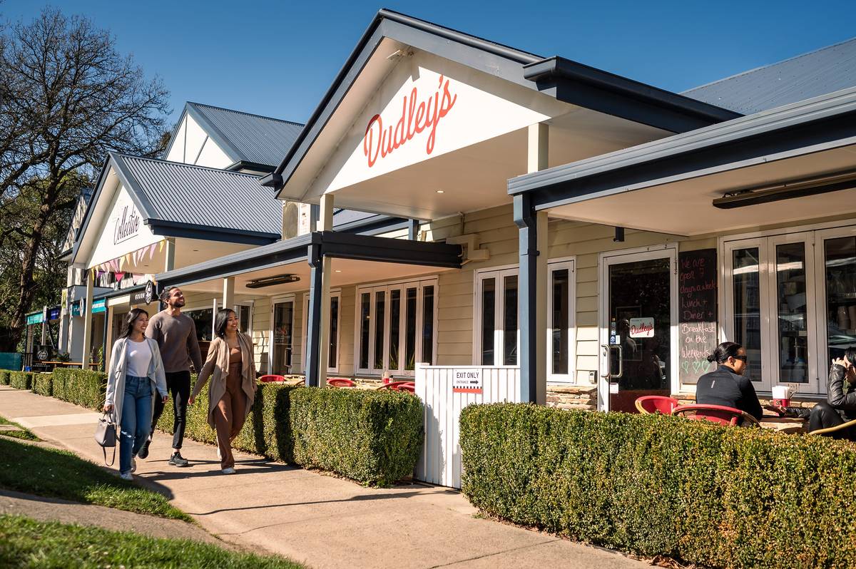 People walking past Dudley’s Café in Olinda, Victoria, with outdoor diners seated under a clear blue sky