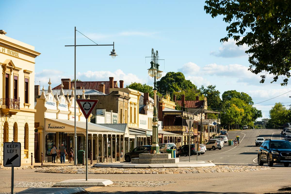 Historic main street in Beechworth, Victoria, with gold rush-era buildings, parked cars, and pedestrians under a clear afternoon sky
