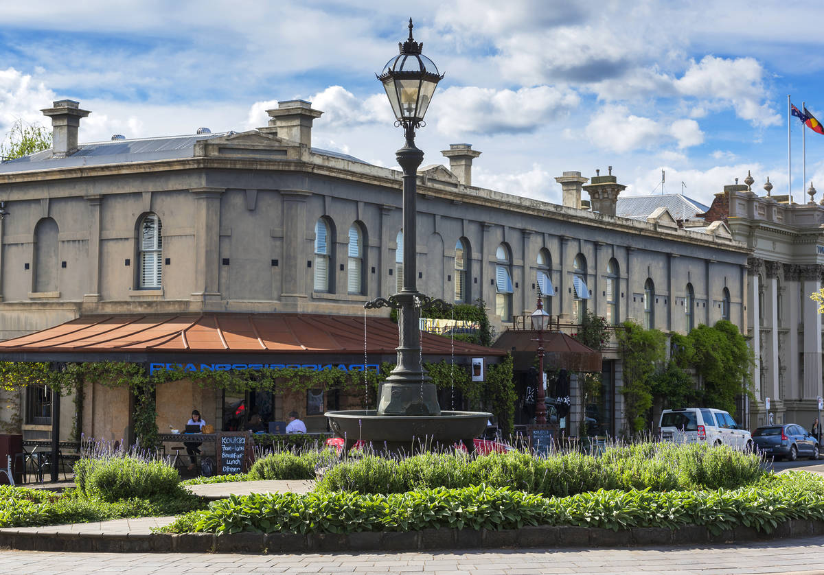 Historic building and central fountain in Daylesford, Victoria, with a leafy cafe terrace and overcast blue skies in the background