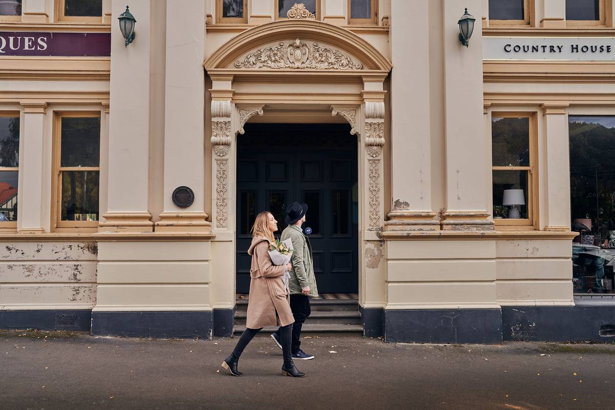 Couple walking past a historic building in Woodend, Victoria, along one of the best main streets in the state, with ornate architecture and vintage shopfronts in view