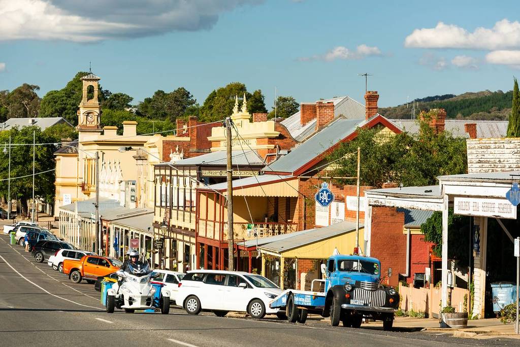 Historic main street in Beechworth, Victoria, with heritage shopfronts, a vintage blue tow truck, and a motorbike under clear afternoon light