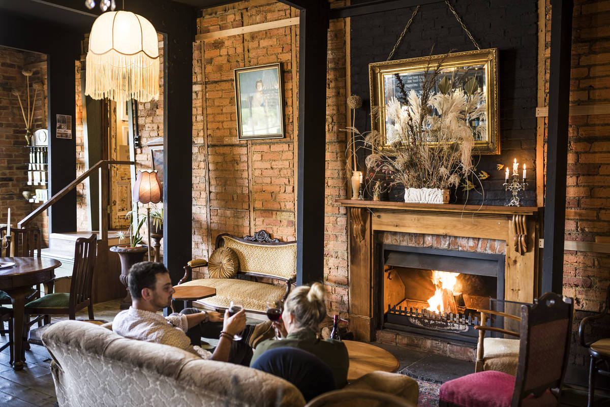 A cosy, inviting cafe in Trentham with exposed brick walls, a warm fireplace, and people relaxing with drinks, creating a comfortable atmosphere