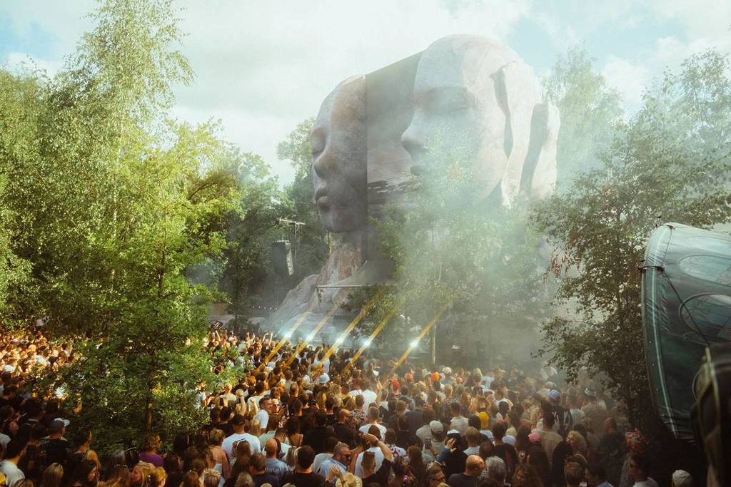 festivalgoers in the forest by a music stage with a face, taken from Tomorrowland CORE in Belgium, to depict what it might be like in Melbourne