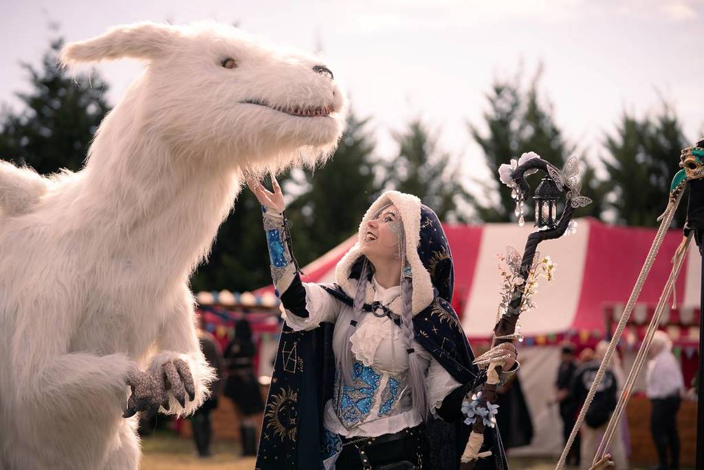 a woman in a winter themed costume looking up at a tall white-furred fantasy creature