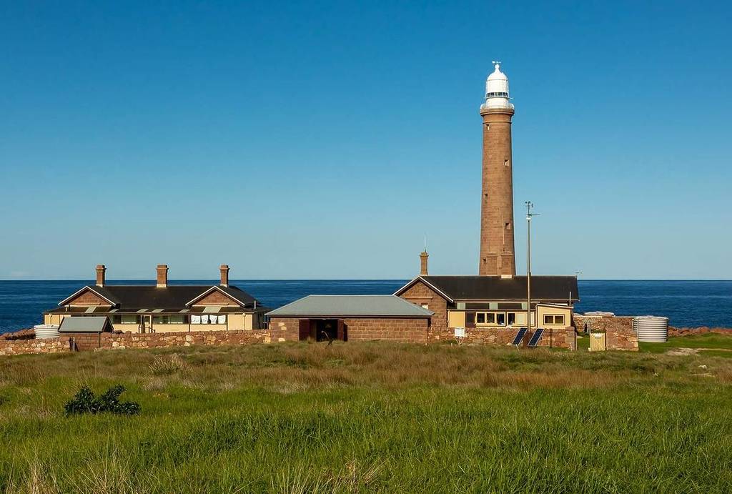 Gabo Island Lighthouse and historic keeper’s cottages set against a bright blue sky, overlooking the ocean on Victoria's remote coastline
