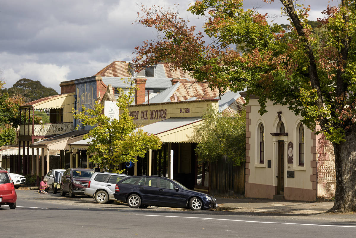 Heritage streetscape in Maldon, Victoria, with vintage shops, iron roofs, and trees lining the street with parked cars