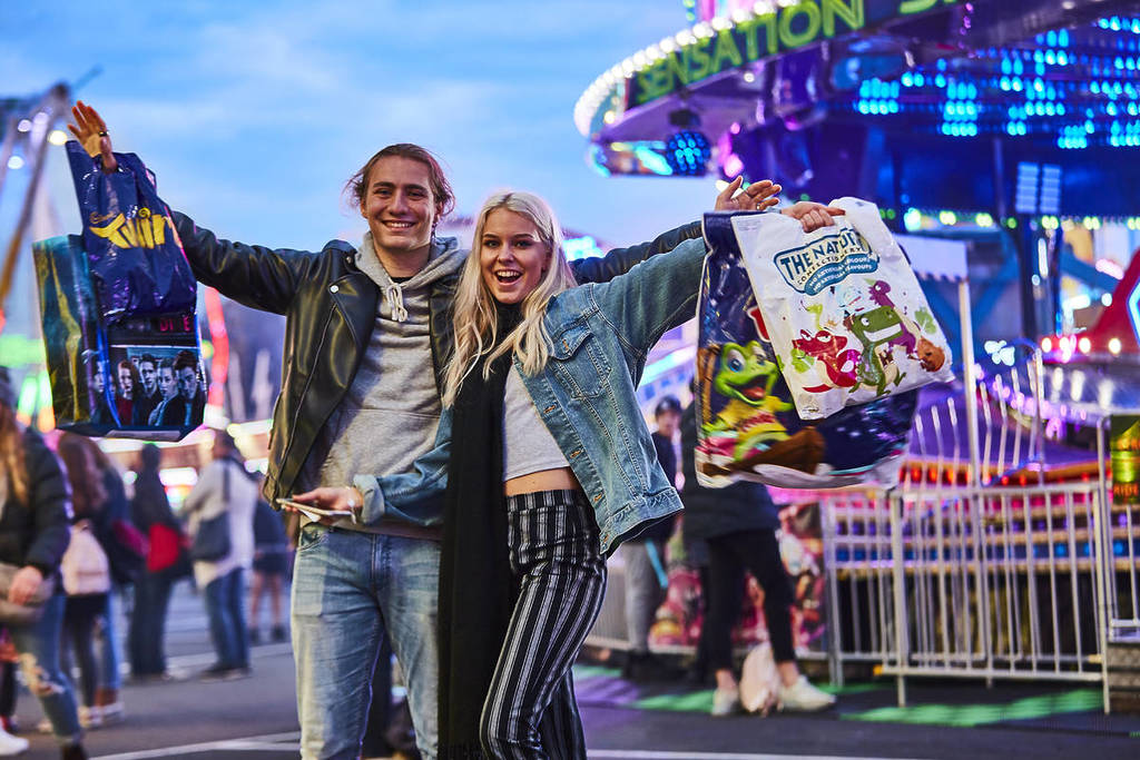 couple holding up showbags in front of rides at Melbourne Royal Show