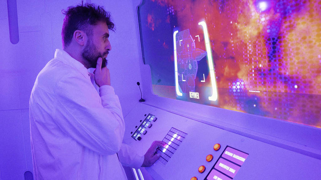 man in white coat holding chin thoughtfully and looking at a screen in the Earthrise One Star Crew escape experience