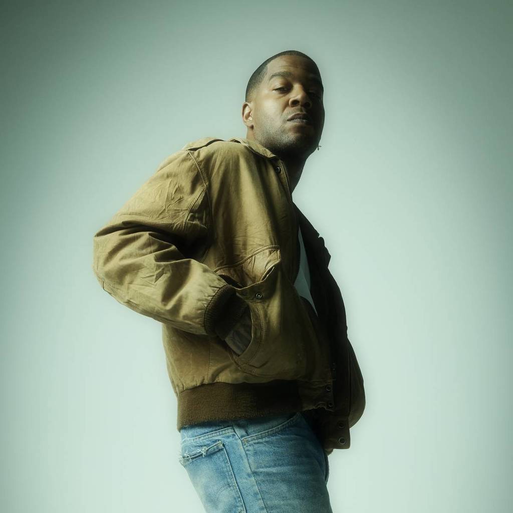 Kid Cudi looking at the camera in a bomber jacket and jeans