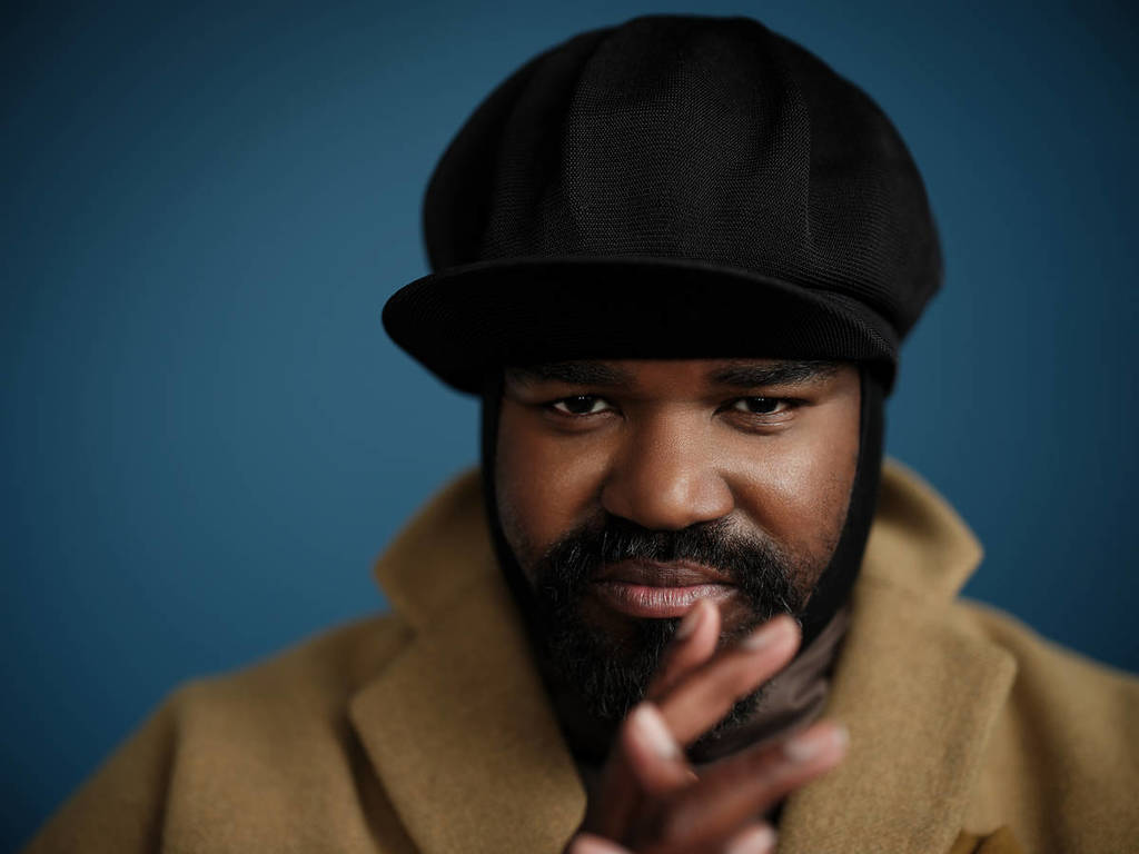 Gregory Porter in a hat and coat looking at the camera