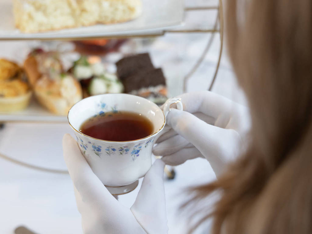 woman in white gloves drinking tea at high tea