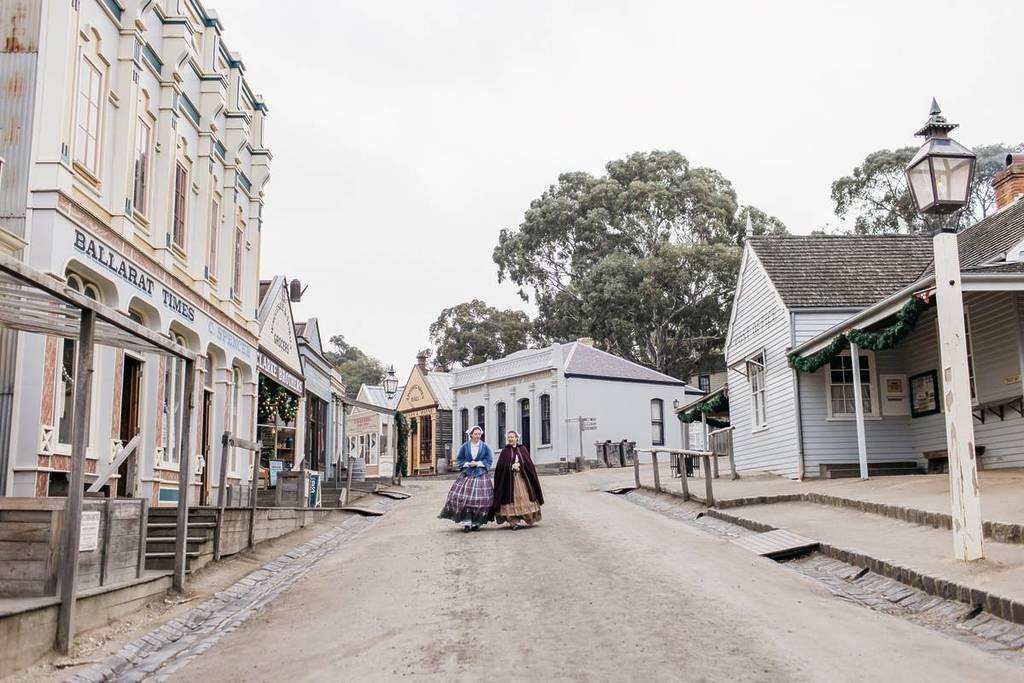 two people in historic costumes walking down a street in Sovereign Hill, one of the things you can do in the gold rush towns of Victoria