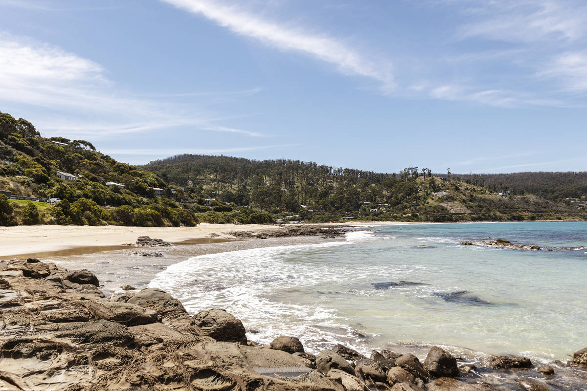 A scenic view of a quiet beach with rocky shoreline and clear waters, framed by hills and coastal homes in the distance in Wye River, one of the most under-the-radar coastal towns in Victoria