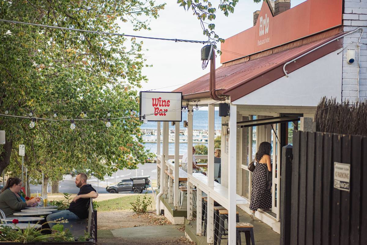 A wine bar in Portarlington with outdoor seating, people enjoying drinks, and a view of the harbour in the background