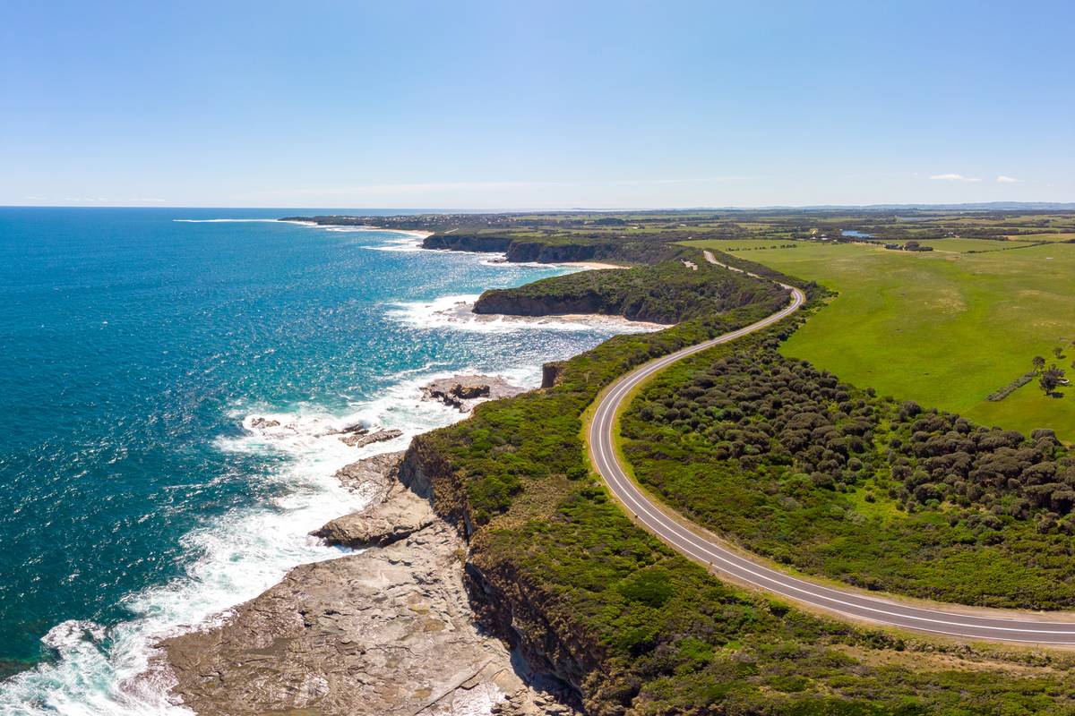 Aerial view of the Bunurong Coastal Drive near Cape Paterson, winding along cliffs above the bright blue ocean