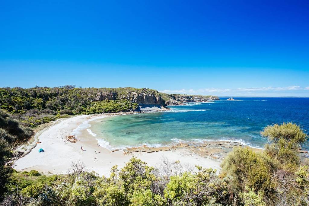 Turquoise bay at Cape Paterson with a small sandy beach, rocky headland, and clear summer skies