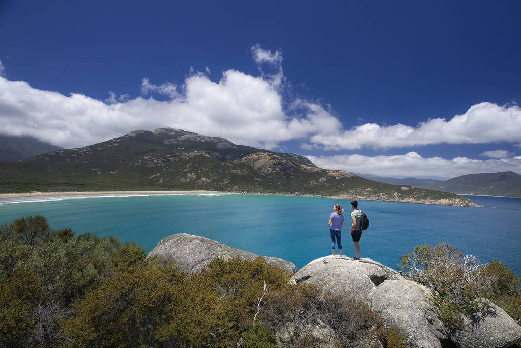 Two hikers standing on large rocks, looking out over the vibrant blue waters and scenic coastline of Wilsons Promontory National Park