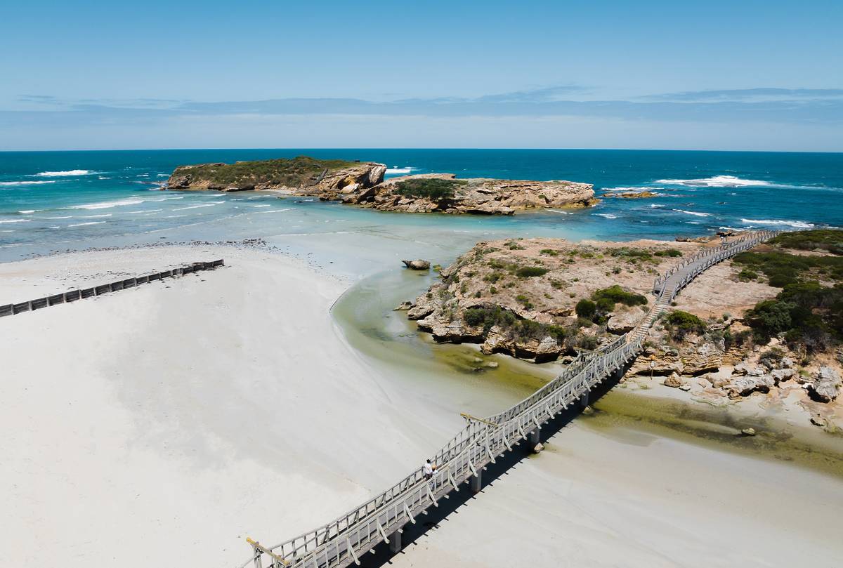 Aerial view of the bridge leading to the rocky coastline with crystal-clear blue waters