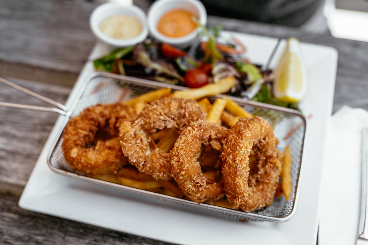 Close-up of a basket of crispy fried calamari rings served with golden fries, a side salad, and dipping sauces at a beachside cafe in Apollo Bay, Victoria