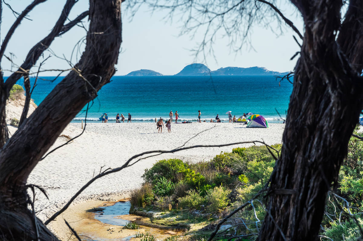 Squeaky Beach in Victoria, featuring white sand, turquoise waters, and visitors enjoying the beach under umbrellas, framed by coastal bushland