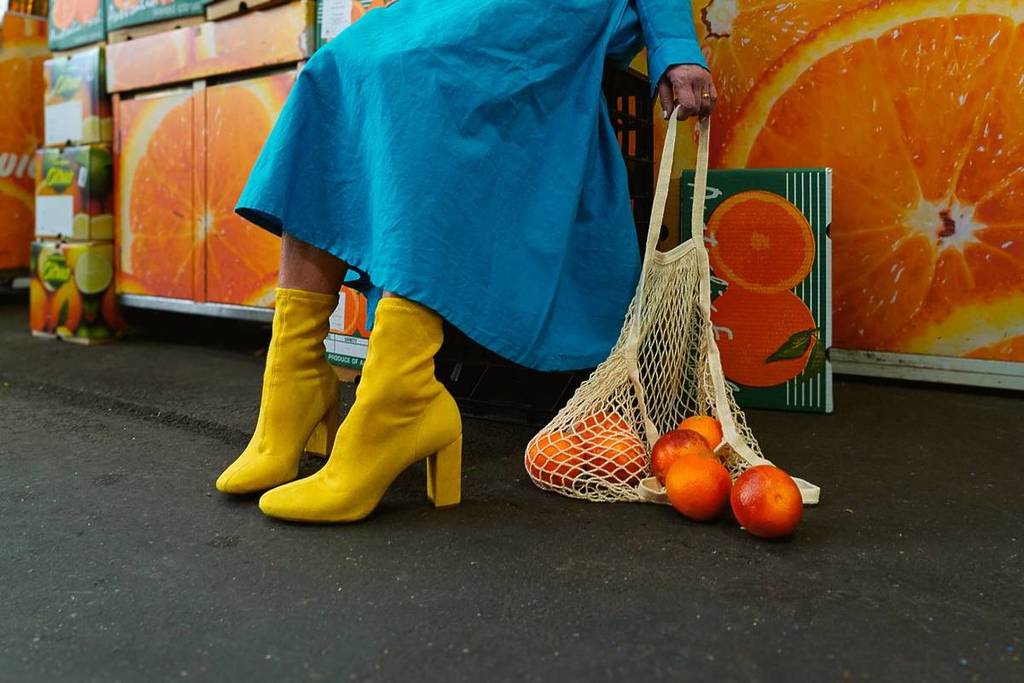 woman in blue dress and yellow heeled boots sitting with a bag of fruit to depict the Revamp fashion market at Prahran Market