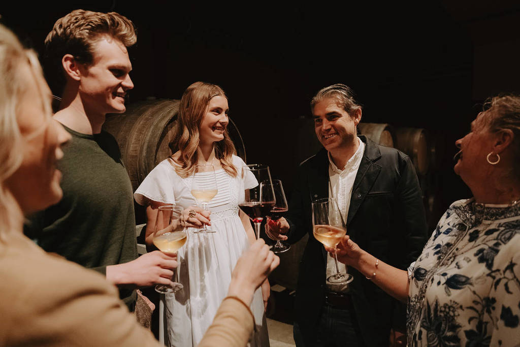 group of people holding wine glasses in a cellar with barrels in the background