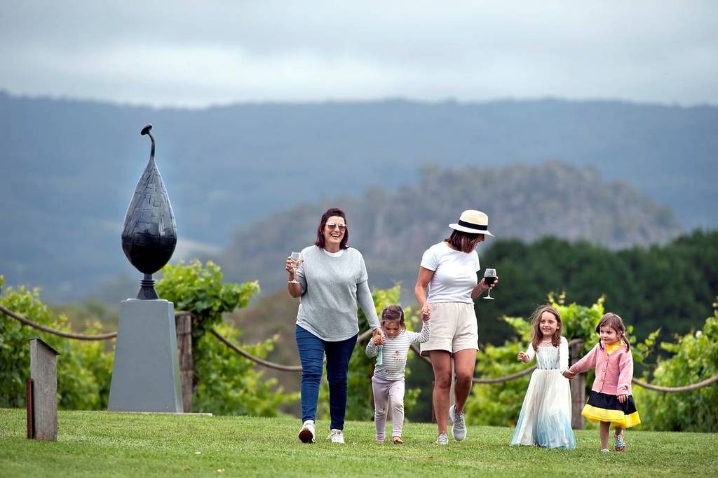 women holding wine glasses walking and holding hands with children with a hilly landscape in the background