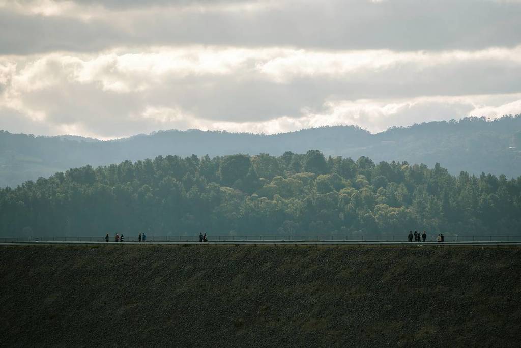people in silhouette up high at Cardinia Reservoir Park, with trees, misty hills and clouds in the distance