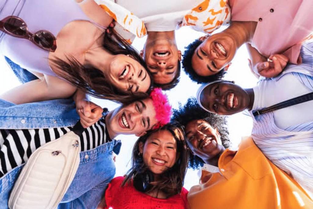 A group of friends with their heads together in a circle look down at the camera.