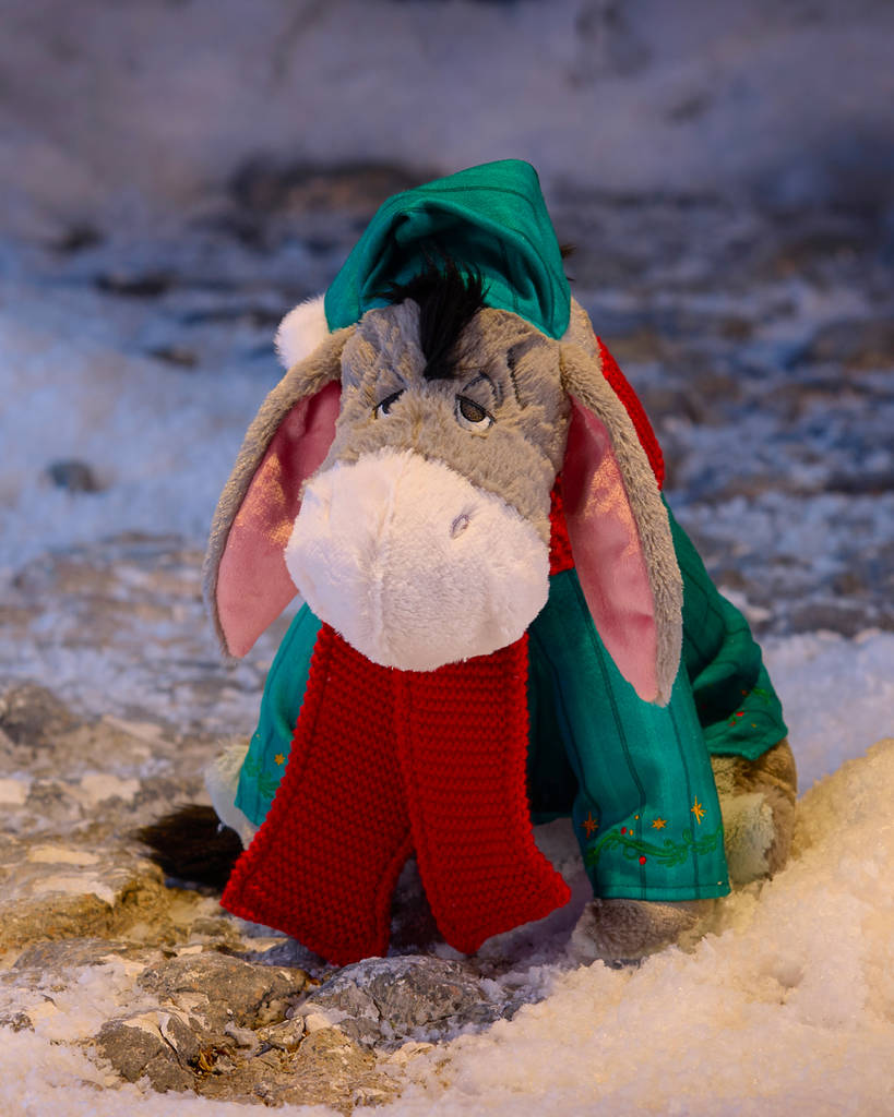 Eeyore plush toy in a festive green hat, red scarf and green jacket