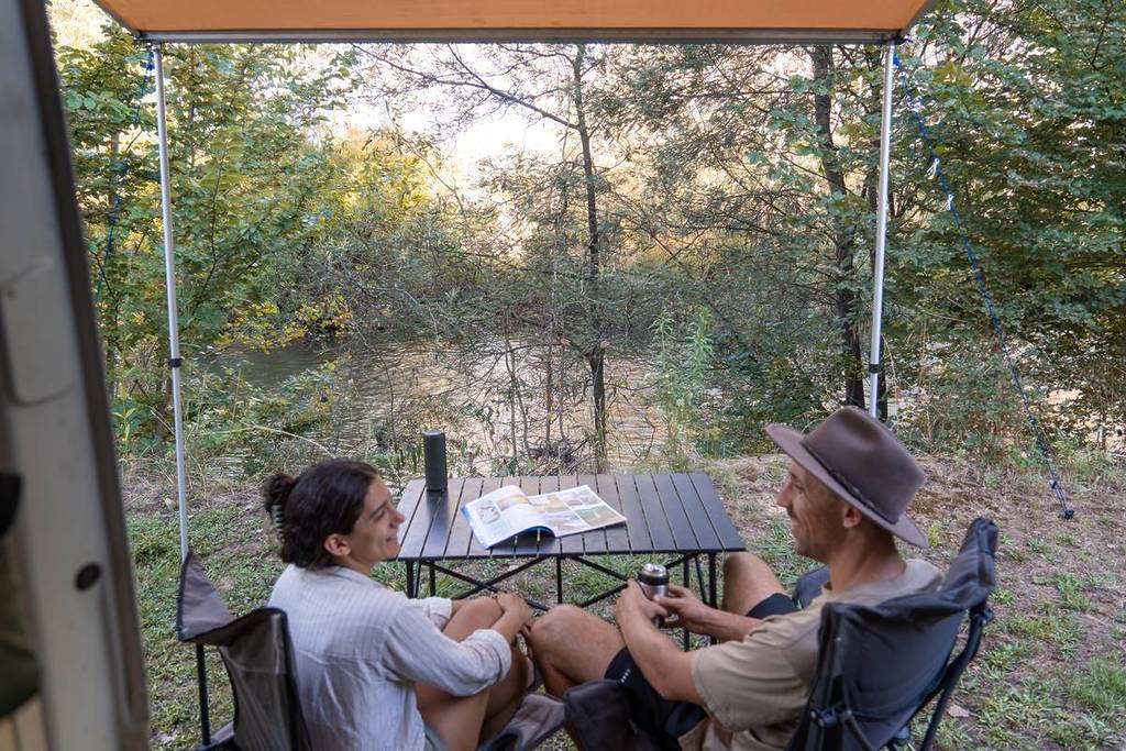 two people sitting by a camping table in front of a river at Riverside King Valley