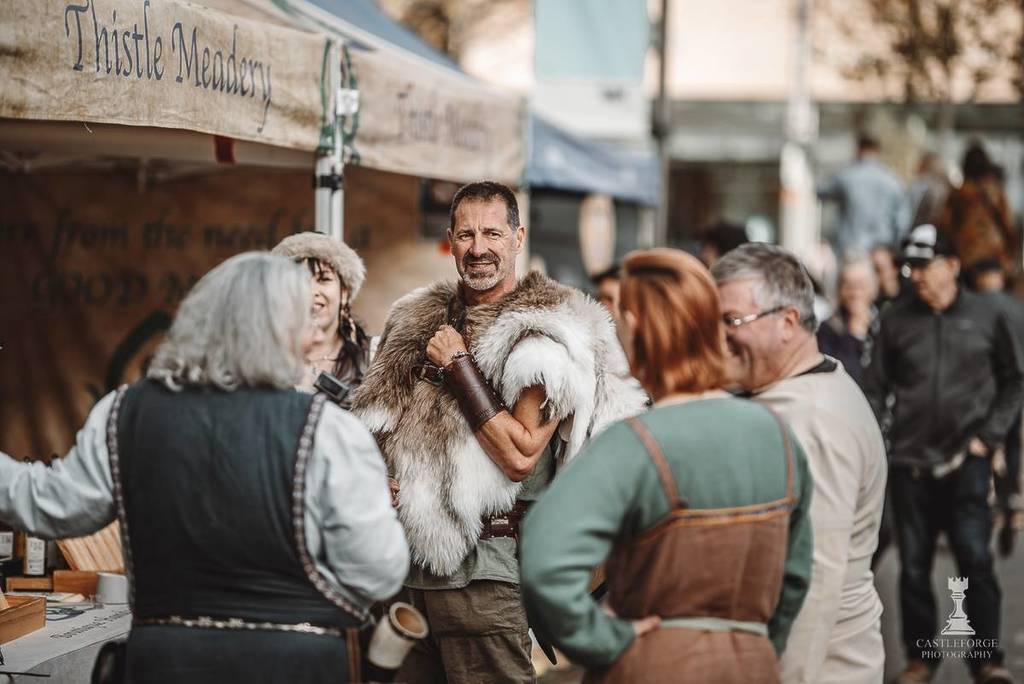 people in medieval outfits in front of a pop-up stall selling mead