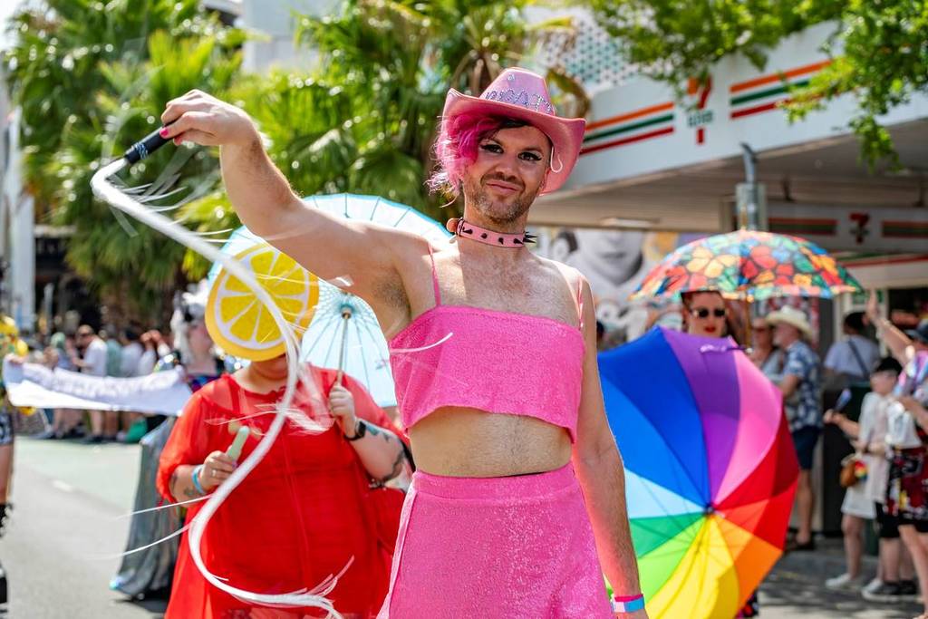 man in pink walking alongside other people dressed in bright colours for Pride March